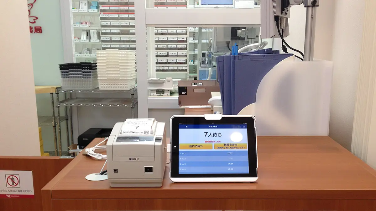 調剤薬局の受付イメージ — 処方箋受付カウンターと調剤完了表示モニター