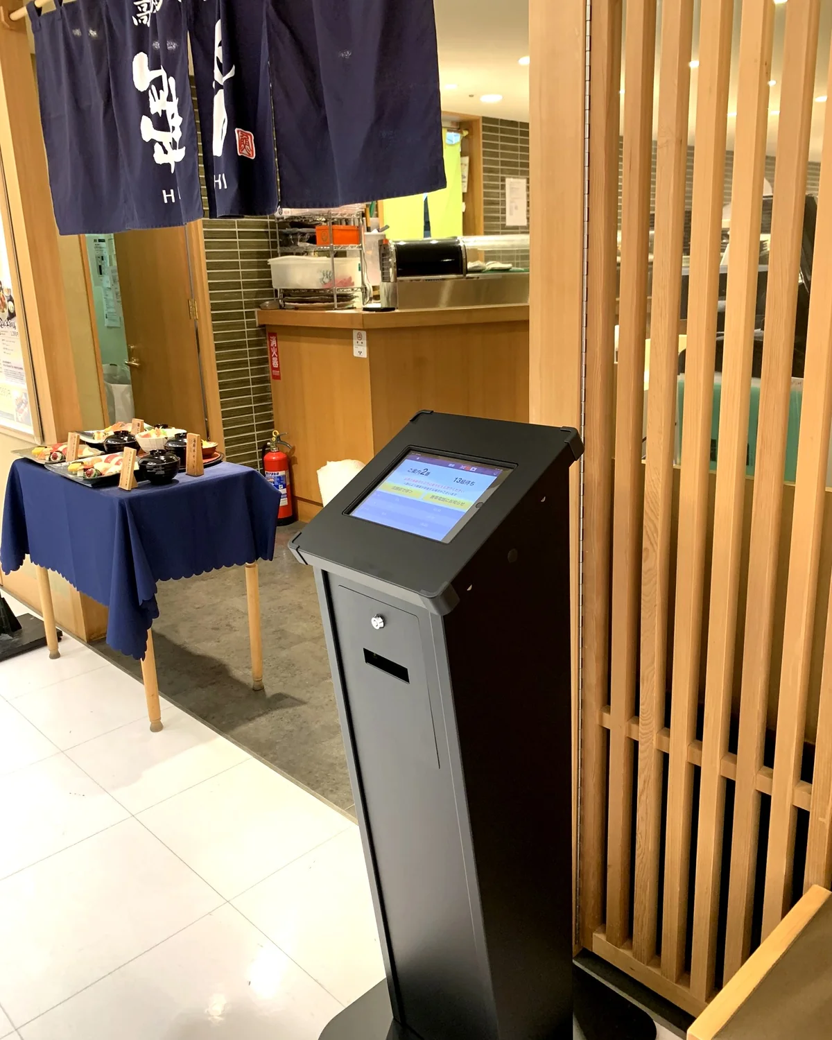 飲食店の入口で順番待ちシステム「アイリスト」発券機が来店客を迎える様子